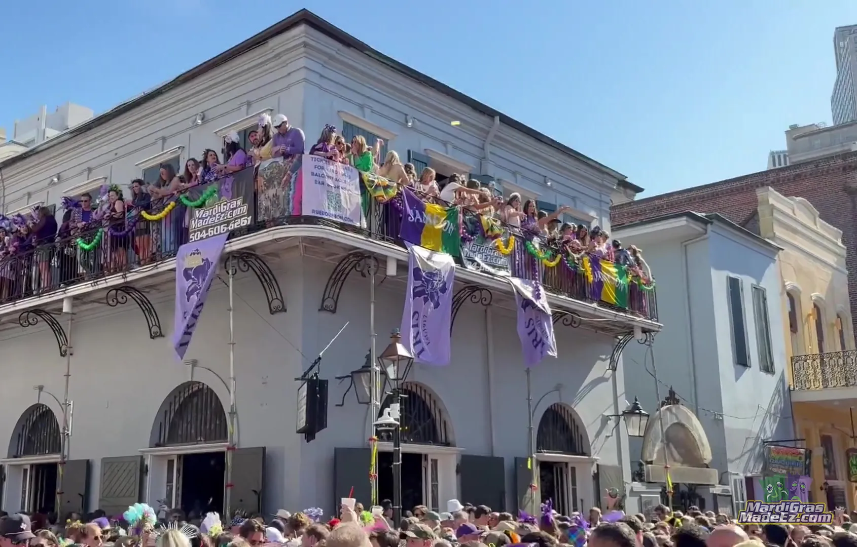 Guests in purple and gold lining a Bourbon Street balcony above the crowd