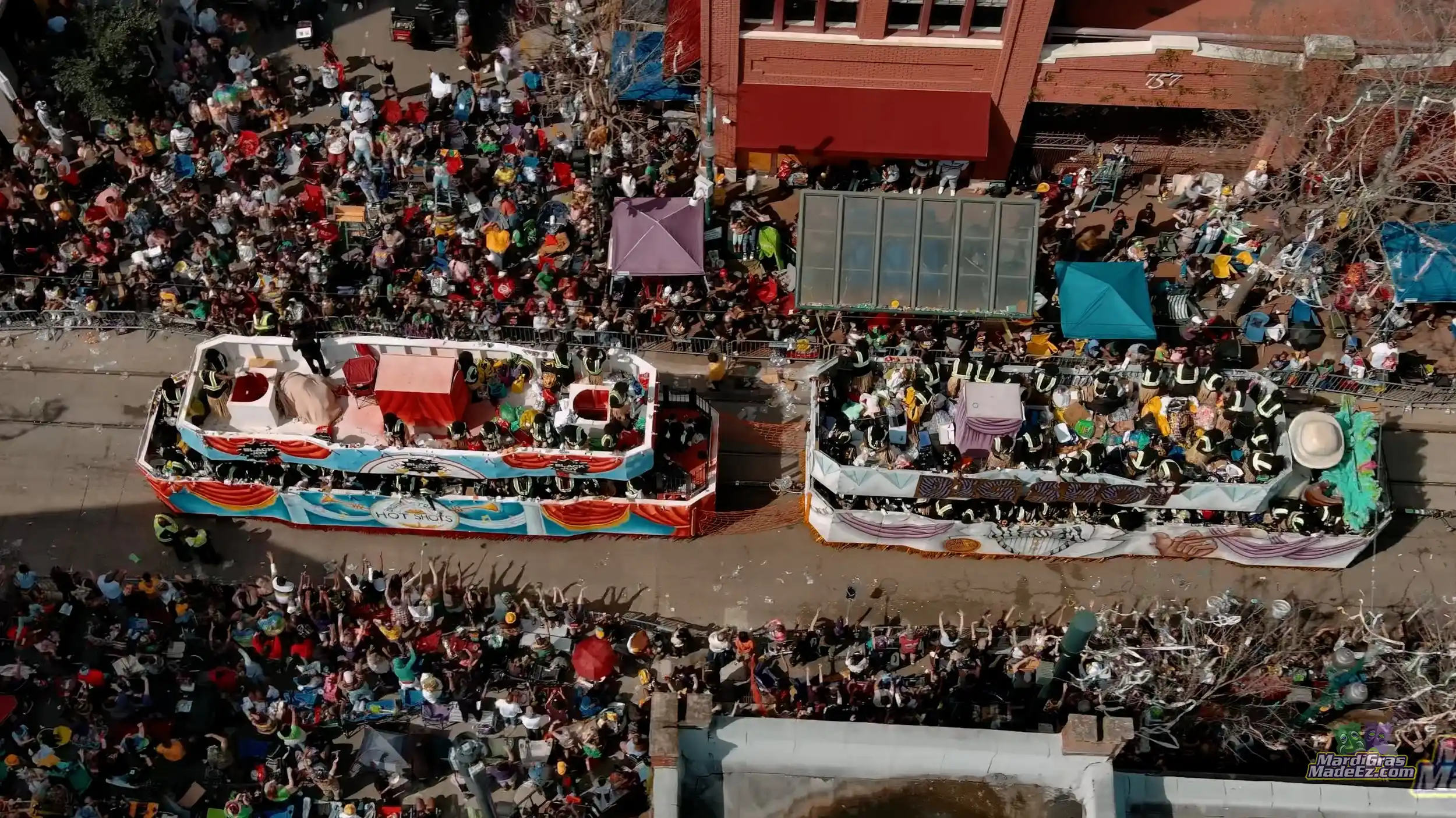 Two Mardi Gras floats rolling past crowds packed along the parade route, seen from above